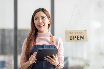 Portrait of a friendly young asian business woman barista wearing apron and standing with her arms crossed at the door of a trendy cafe, open sign barista SME entrepreneur seller concept