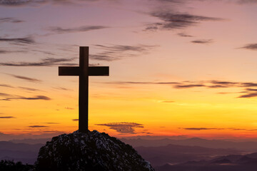 Christian cross on top rock mountain with bright sunbeam on the colorful sky background. Christian background concept