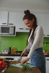 Vertical shot of cheerful young pretty female cooking in kitchen at cozy apartment