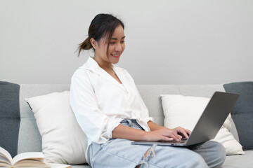 Naklejka premium Portrait of a young Asian woman sitting on the sofa using a computer.
