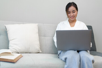 Naklejka premium Portrait of a young Asian woman sitting on the sofa using a computer.