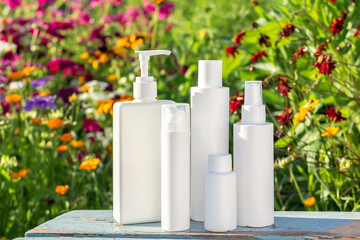 Set of cosmetic for skin care face, body on bright floral background. White blank cosmetics bottles, jar and stones. Natural Organic Spa Cosmetic Beauty Concept Mockup Front view