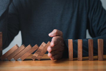Hand Stopping the domino business crisis effect or risk protection concept, business solution and intervention, Wooden tower falling concept.