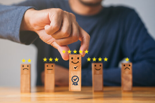 Quality assurance, Guarantee, Standards, ISO certification. excellent business services rating customer experience. Satisfaction survey. Hand of a businessman chooses a smiley face on wood block.