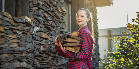 Woman is putting wood in hands from a woodpile for a home fireplace. Wood-burning heating and the energy crisis
