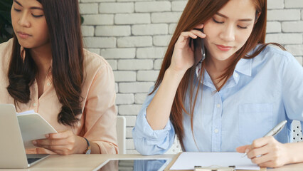 Two businesswomen team meeting using laptop at company office desk. Two young Female freelance reading financial graph charts Planning analyzing marketing data. Asian people team working office firm.