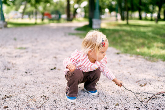 Little girl squats on the gravel with a branch. High quality photo