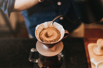 Professional barista making filtered drip coffee in coffee shop. Close up of hands barista brewing a drip hot espresso coffee, pour over coffee with hot water and filter paper in coffee cafe.
