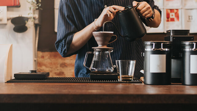 Professional barista making filtered drip coffee in coffee shop. Close up of hands barista brewing a drip hot espresso coffee, pour over coffee with hot water and filter paper in coffee cafe.