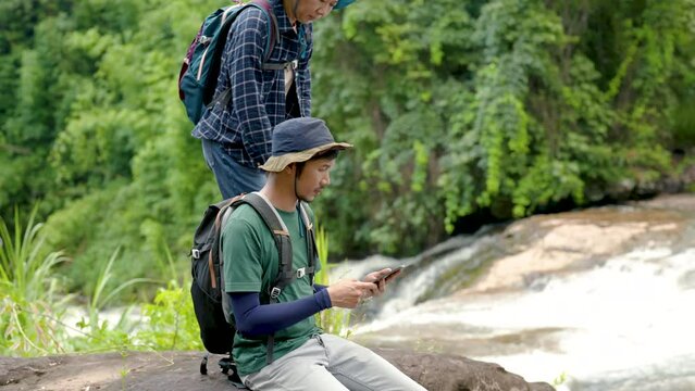 4K, Asian man, and woman sitting with laptops open, Let's look at the directions, on the map with the laptop in hand, so that it's convenient to hike here, and the two of them sat on the rocks.