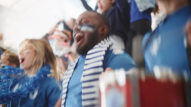 Sport Stadium Big Event: Handsome Black Man Cheering. Crowd of Fans with Painted Faces Cheer, Shout for their Blue Soccer Team to Win. People Celebrate Scoring a Goal, Championship Victory.