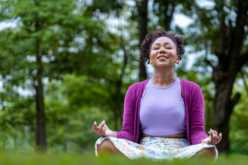 African American woman relaxingly practicing meditation in the forest to attain happiness from...
