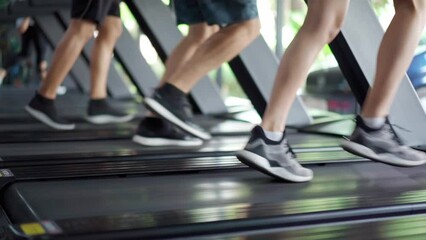 Close-up side view of leg and feet in sneakers of young fitness people, men and women, having workout by running on the treadmill in a fitness gym or sport club. Exercise and Healthy lifestyle concept