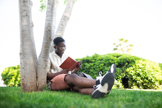 African american university student relaxing on campus.Young black man reading book outdoors.