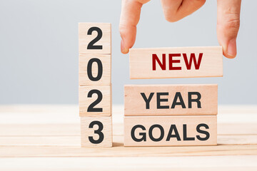 hand holding wooden block with text 2023 NEW YEAR NEW GOALS on table background. Resolution,...