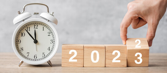 Happy New Year with vintage alarm clock and hand flipping 2022 change to 2023 block. Christmas, New...