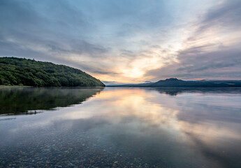 Fototapeta na wymiar 空を湖面に反射する夜明けの湖。日本の北海道の屈斜路湖。
