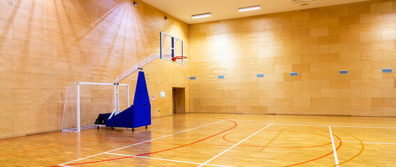 In yellow light, a basketball gym with a mobile basket without people