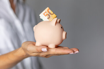 female hands put euro money in a pink piggy bank. The concept of saving money or savings, investment