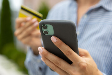 female hands hold a modern mobile phone and a bank credit or debit card on the street..ordering purchases, working online, transferring money by phone