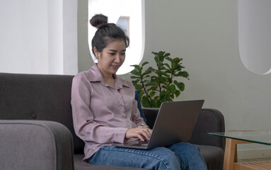 Young business freelance Asian woman working on laptop checking social media while lying on the sofa when relax in living room at home. Lifestyle latin and hispanic ethnicity women at house concept.