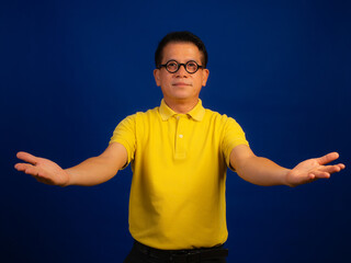 Portrait of smiling middle-aged asian man in casual yellow polo shirt with welcoming gesture...