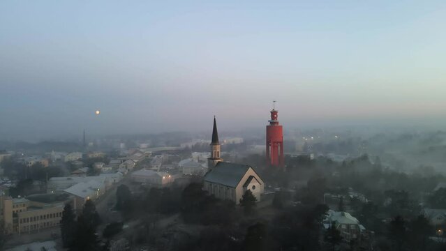 Aerial view in front of the church and watertower, foggy, spring morning in Hanko, Finland - pan, drone shot