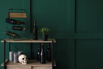 Shelving unit with wine bottles, human skull and candles near green wall