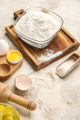 Wooden board with bowl of flour and chicken eggs on light background