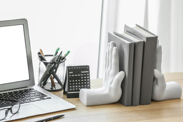 Stylish holder with books, calendar, pen cup and laptop on table near window