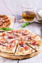 French tarte flammkuchen with cream cheese, onion and bacon on a board on the table. Vertical view