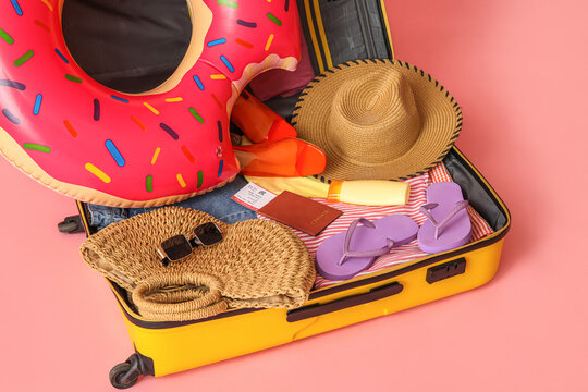 Open suitcase with clothes, beach accessories and passport on pink background, closeup