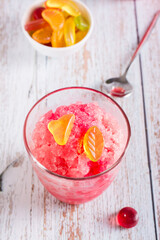 Red shaved ice snow cone with syrup and sweets in glasses on the table. Vertical view. Closeup