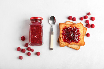Tasty toasts with raspberries, jar of jam and spoon on white background
