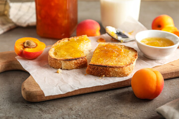 Board with tasty toasts and apricot jam on grunge background, closeup