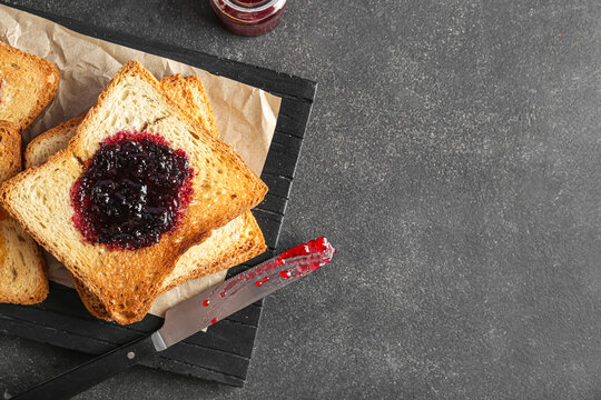 Wooden board of toasts with sweet jam on dark background