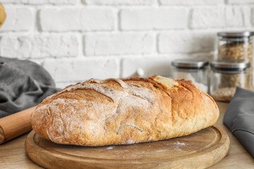 Board with loaf of fresh bread on kitchen counter near white brick wall