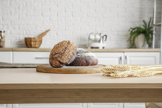 Cutting board with loaves of fresh bread on table in kitchen