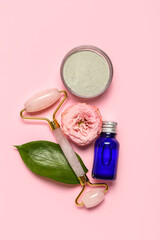 Facial massage tool with cosmetic products and flower on pink background