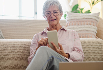 Senior woman sitting on the floor at home while reading a message on mobile phone, elderly lady enjoying technology and communication