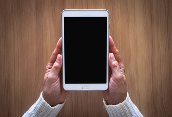 Mature female hands holding the white tablet pc computer with blank screen isolated on desk background