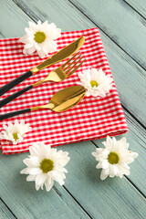 Cutlery, napkin and chamomile flowers on color wooden background