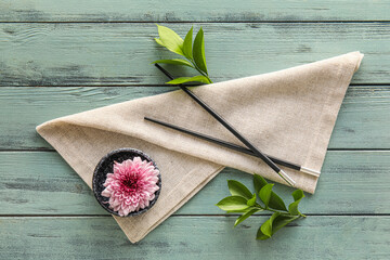 Bowl with chrysanthemum flower, chopsticks and napkin on color wooden background