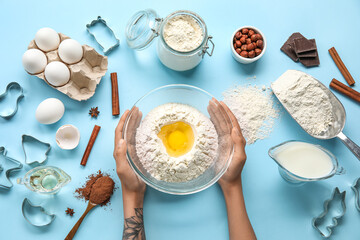 Female hands with ingredients for preparing cookies and cutters on color background