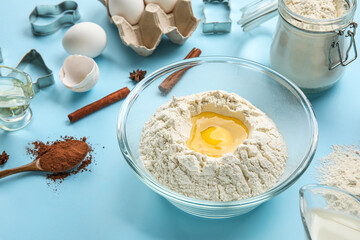 Glass bowl with flour and egg on color background