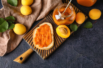 Wooden board of tasty sandwich with apricot jam and fruits on dark background