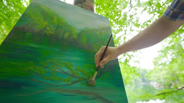 The painter paints in the forest.
The painter paints the landscape of nature on his canvas.
