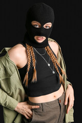 Young woman in balaclava with hands in pockets on black background