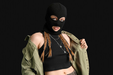 Young woman in balaclava touching shirt on black background