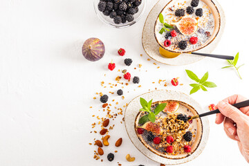 breakfast for two. cooked delicious granola in ceramic bowls with nuts, berries, mint and figs. a woman's hand holds a spoonful of muesli.